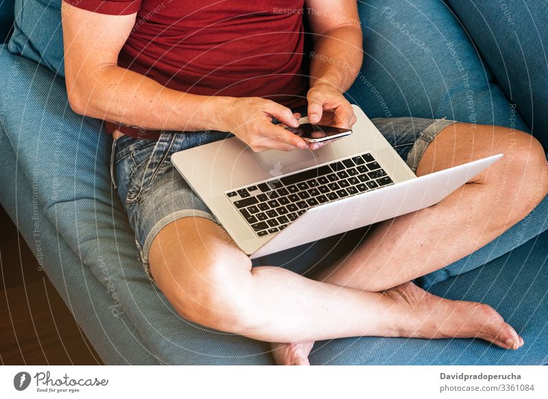 anonymer Mann tippt auf Smartphone, während er sich zu Hause mit Laptop ausruht Kälte Armsessel heimwärts ruhen Freund Wohnzimmer Lifestyle benutzend Mobile