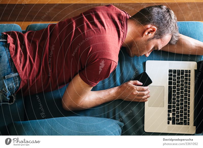 Müde Kerl schlafen auf Sofa mit Geräten zu Hause Mann schlafend Liege müde freiberuflich Wohnzimmer überarbeitet Smartphone Mobile Telefon Laptop erschöpft
