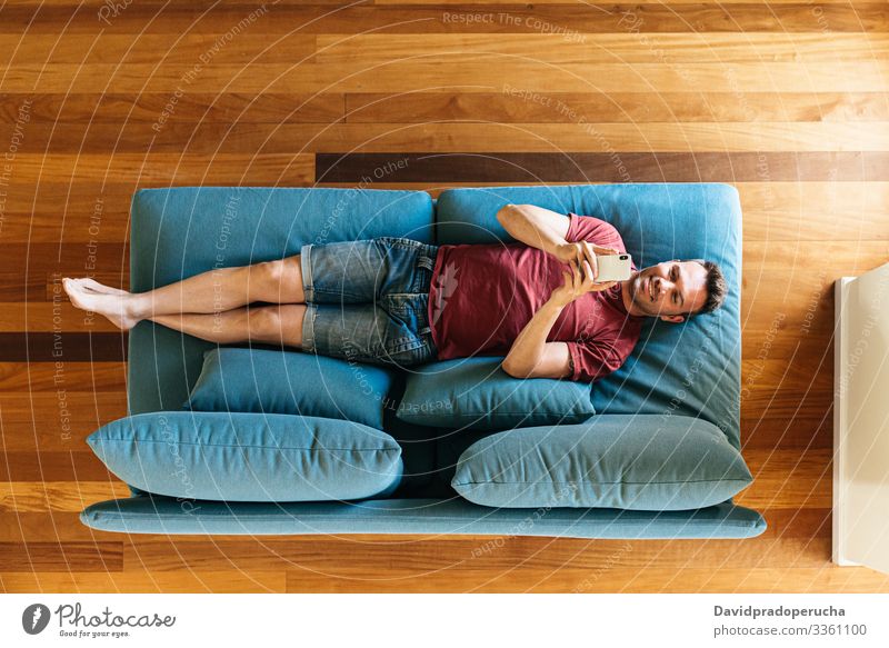Lässiger Typ auf Sessel mit Smartphone Mann benutzend Armsessel Browsen Wohnzimmer Komfort Surfen Kälte räkeln Texten zuschauend Anschluss soziale Netzwerke