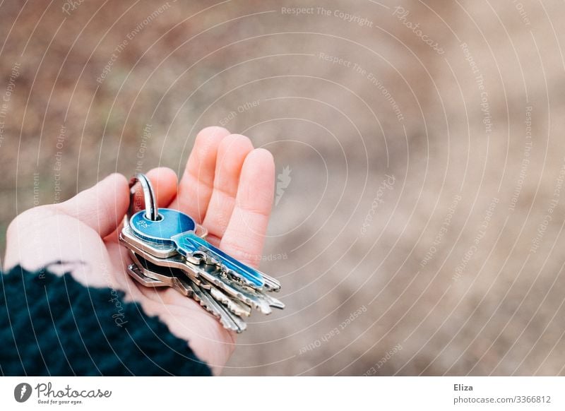 Eine Hand die einen Schlüsselbund mit einem blauen Schlüssel daran bei der Wohnungsübergabe nach einem Umzug übergibt. Konzept Wohnen, Wohnraum und Schlüsselübergabe.