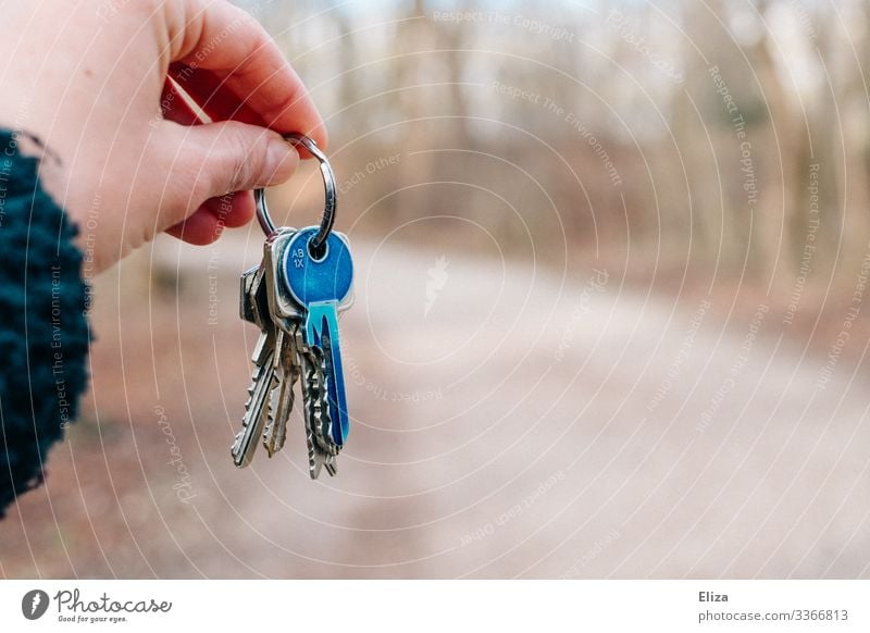 Eine Hand die einen Schlüsselbund mit einem blauen farbigen Schlüssel festhält, übergibt, überreicht geben festhalten schlüsselübergabe Wohnung vermieten