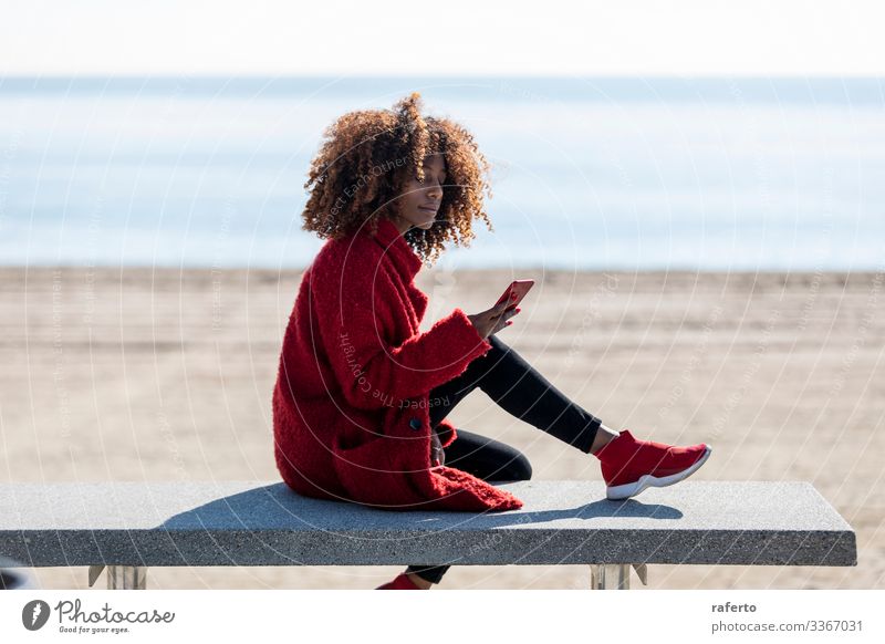 Schöne Afro-Frau sitzt an der Küste und benutzt ein Mobiltelefon Stil Glück schön Strand Telefon PDA Mensch feminin Junge Frau Jugendliche Erwachsene 1