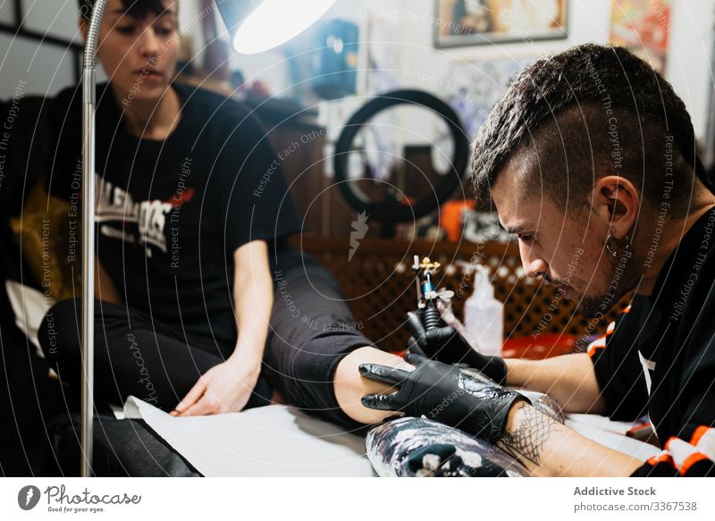 Tätowierer bei der Arbeit mit Kunden im Salon Klient Mann Tattoo Werkzeug stylisch Subkultur Künstler Kultur Meister kreativ Mode professionell modern
