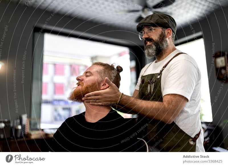 Barbier macht Gesichtsmassage beim Mann Klient trendy Friseur Barbershop Vollbart Maskulinität jung Pflege Salon gutaussehend stylisch entspannend Stressabbau