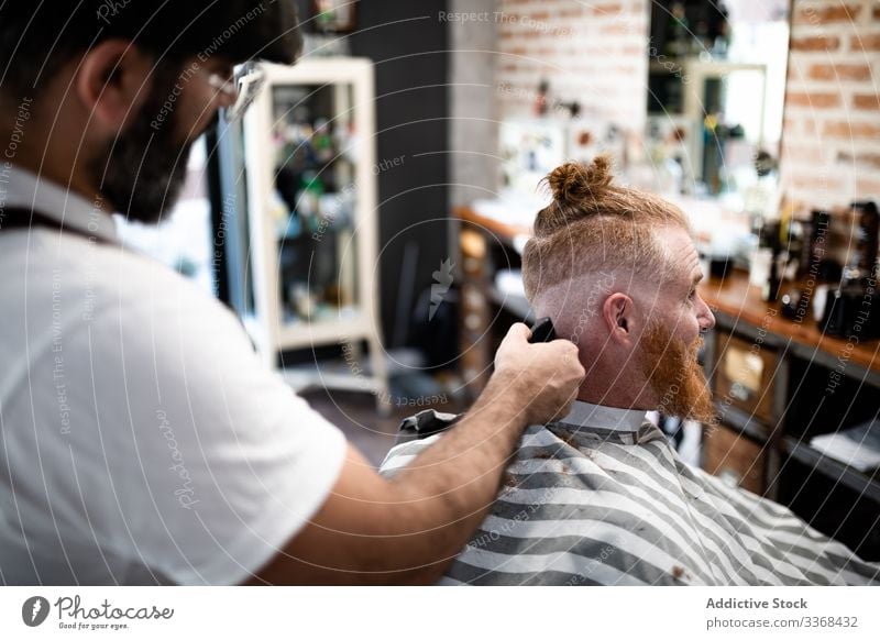 Friseur schneidet einem rothaarigen Mann die Haare Klient trendy Barbershop bärtig Maskulinität Kunde Behaarung Pflege Salon Hipster gutaussehend stylisch