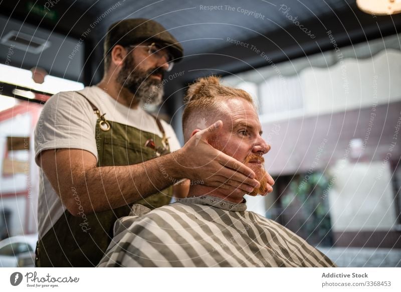 Barbier macht Gesichtsmassage beim Mann Klient trendy Friseur Barbershop Vollbart Maskulinität jung Pflege Salon gutaussehend stylisch entspannend Stressabbau