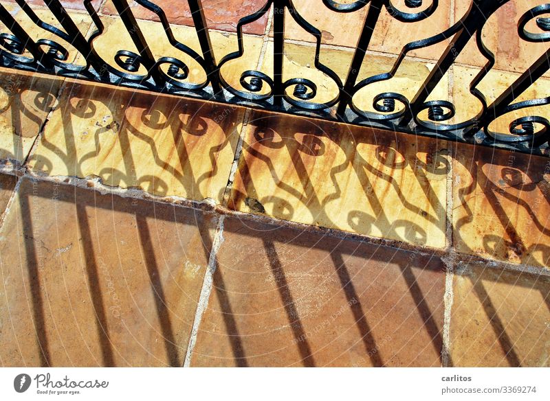 Schmiedeeisernes Tor mit Schattenwurf auf Terracottaplatten Spanien Balearen Mallorca schmiedeeisen Metall Verzierung Schnörkel Sonnenlicht Platten Fliesen Rost