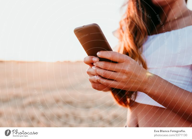 Unkenntnis einer jungen schönen Frau auf dem Land bei Sonnenuntergang mit dem Handy. technologiekonzept unkenntlich Technik & Technologie Porträt im Freien