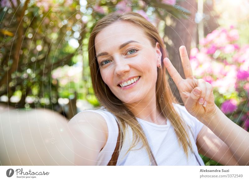 Schöne Frau, die im Tropenwald mit Blumen reist, auf einem Holzpfad spazieren geht, Selfie-Fotos macht und dabei glücklich lächelt. Touristin mit Rucksack mit Friedenszeichen