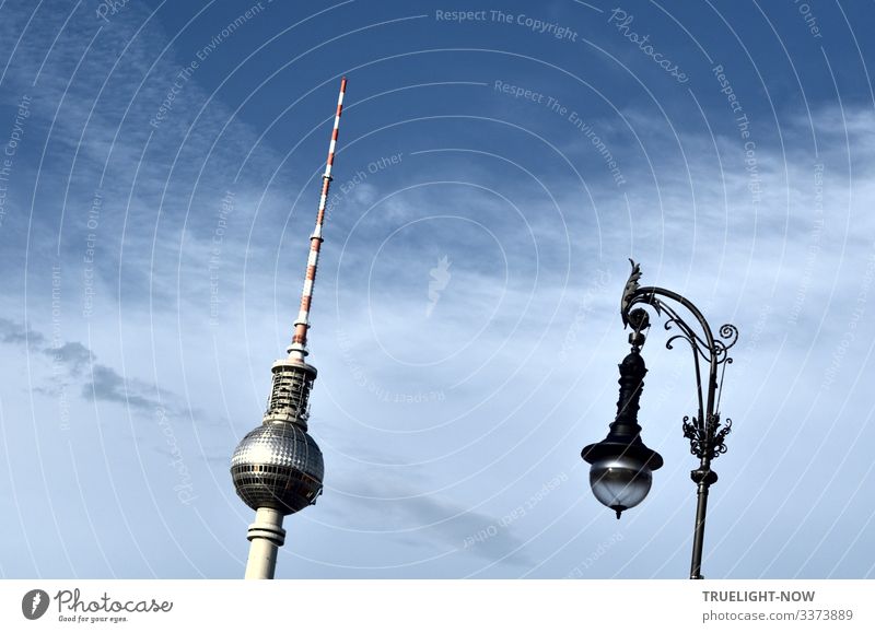 Berliner Fernsehturm am Alexanderplatz und Straßenlaterne im historischen Stil parallel und das Sonnenlicht reflektierend gegen den blauen Himmel mit teilweise leichter Wolkendecke