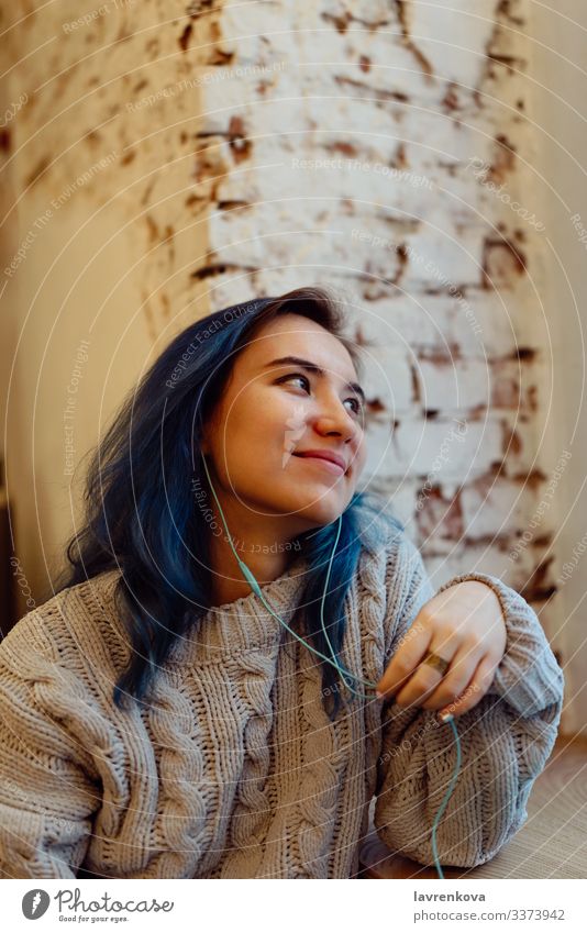 Junge erwachsene Frau mit gefärbten blauen Haaren hört Musik in einem Café während der blauen Stunde, flacher selektiver Fokus Erwachsene Asiate