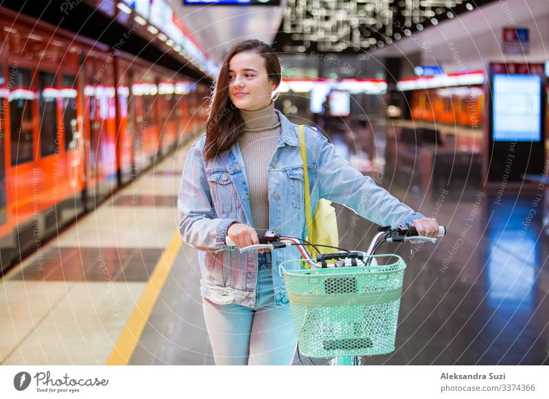 Teenager mit Rucksack und Fahrrad auf der U-Bahn-Station stehend, Smartphone in der Hand haltend, blätternd und simsend, lächelnd und lachend. Futuristisch helle U-Bahn-Station. Finnland, Espoo