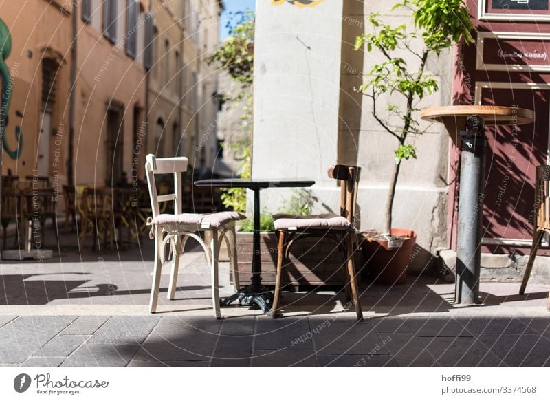 zwei alte unterschiedliche Holzstühle mit kleinem Tisch vor einem Bistro in den Strassen von Marseille Sonnenlicht Schönes Wetter Wärme Baum Haus Restaurant
