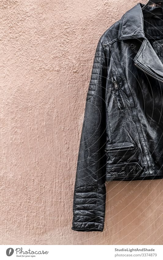 Schwarze Lederjacke an rosa Wand schwarz Jacke Reißverschluss Tasche Mode Stil stylisch glänzend cool Felsen Rocker Metall Schwermetall Bekleidung Kleidung