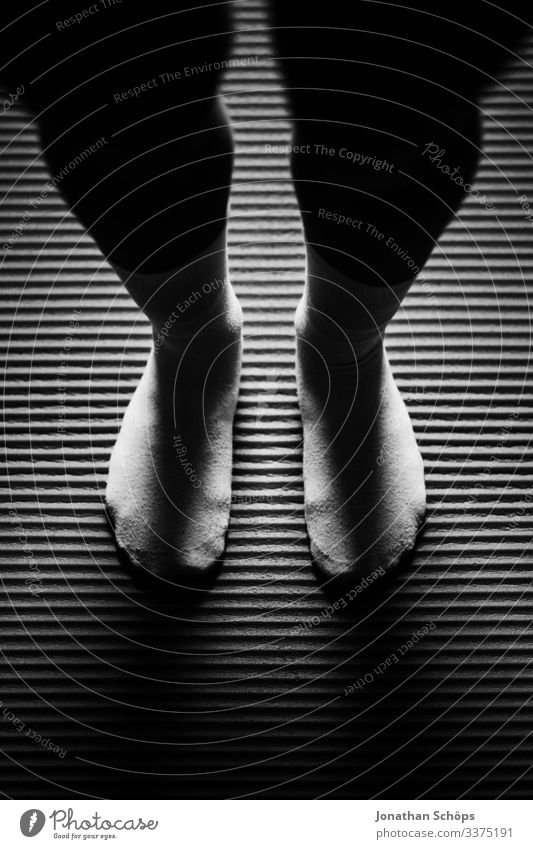 Frau steht achtsam mit Socken auf Yogamatte Abstrakter schwarzer Hintergrund Beine Darkmode Fitness Füße Isomatte Leggings Minimales Schwarz Minimalismus