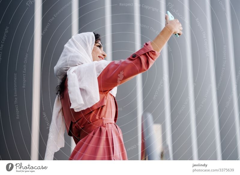 Arabische Frau mit Hidschab, die sich mit einem Smartphone selbstständig macht arabisch Hijab muslimisch jung Foto Selfie Schal schön urban Großstadt Lifestyle