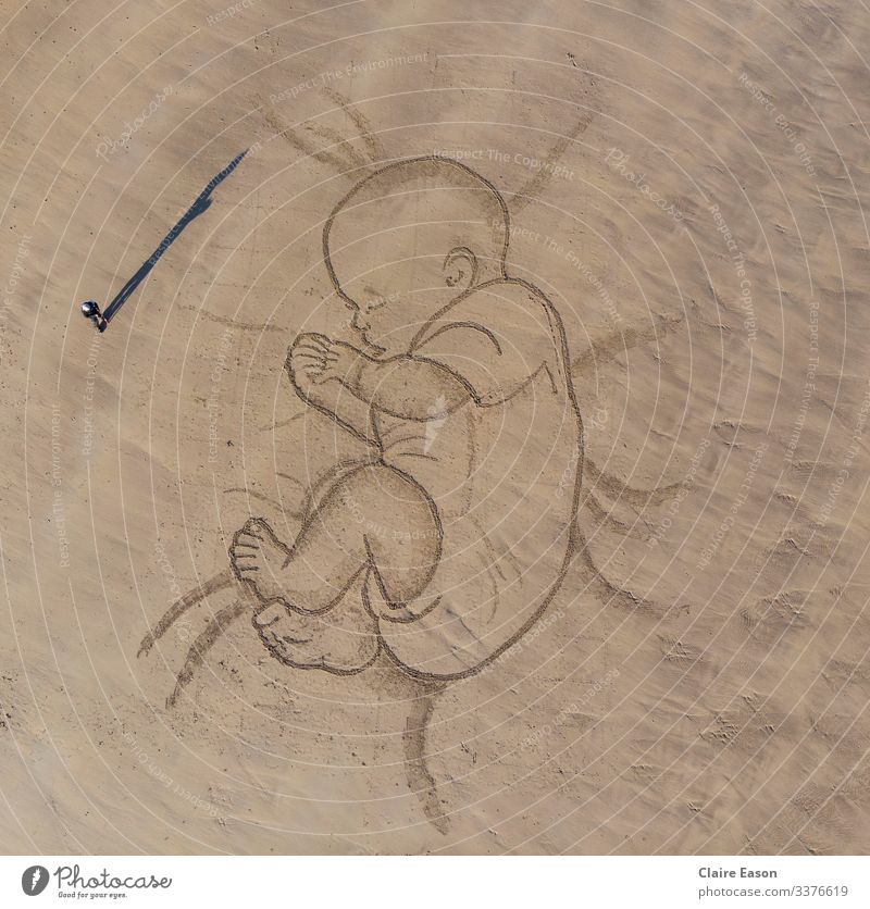 Riesige Sandkunstzeichnung eines schlafenden Babys mit Person für den Maßstab Riese Zeichnung schlafendes Baby friedlich Elternschaft Familie Strand Küste