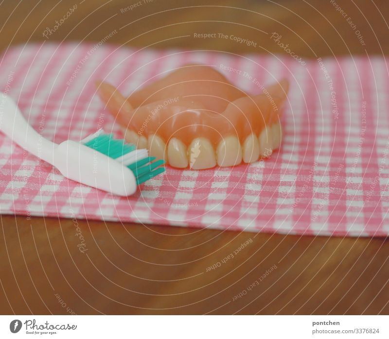 Zahnprothese und Zahnbürste liegen auf kariertem Stoff auf Holztisch Zähne retro Sauberkeit Serviette rosa Nachbildung lernen üben Karies Schutz Zahnarzt