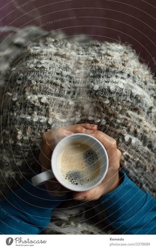 Eine mit einer Decke bedeckte Frau genießt an einem kalten Tag ein heißes Getränk. Milcherzeugnisse Frühstück Kaffeetrinken Slowfood Heißgetränk Latte Macchiato