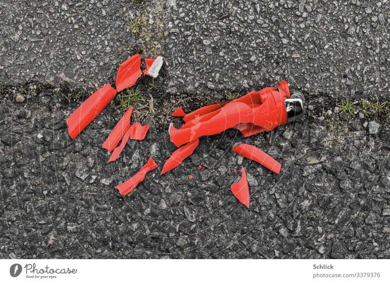 Zerbrochenes rotes Einwegfeuerzeug auf Asphalt zerfällt in Mikroplastik Umwelt Feuerzeug Metall Kunststoff grau schwarz silber Umweltverschmutzung Konsum