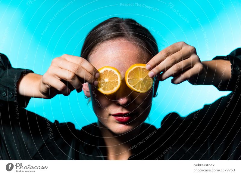 Kaukasische Frau, die ihre Augen mit Zitronenscheiben auf blauem Hintergrund bedeckt Scheibe deckend Mädchen Überfall Konzept Minimalismus Zitrusfrüchte Frucht