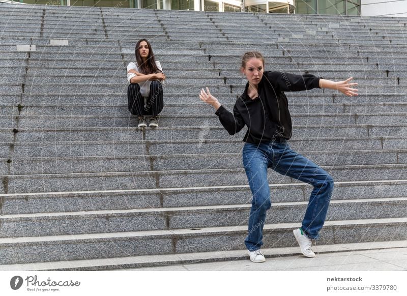 Junge Frau tanzt und eine andere sitzt auf Marmortreppen Sitzen Tanzen Frauen Mädchen Freitreppe Treppenhaus junger Erwachsener Jugendkultur Tag urban