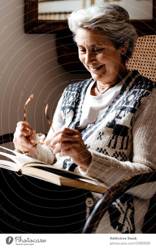 Ältere Frau lächelt mit Brille und aufgeschlagenem Buch auf Knien im Sessel Lächeln älter Literatur Konzentration Information intelligent klug kreativ
