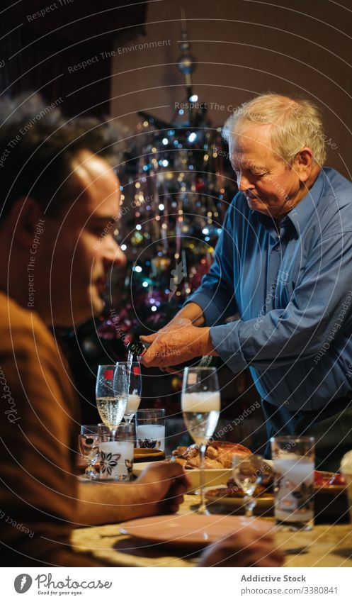 Alter Mann schenkt beim Weihnachtsessen zu Hause Champagner in Gläser ein Weihnachten feiern heimwärts Flasche Glas gealtert Senior lässig trinken Getränk