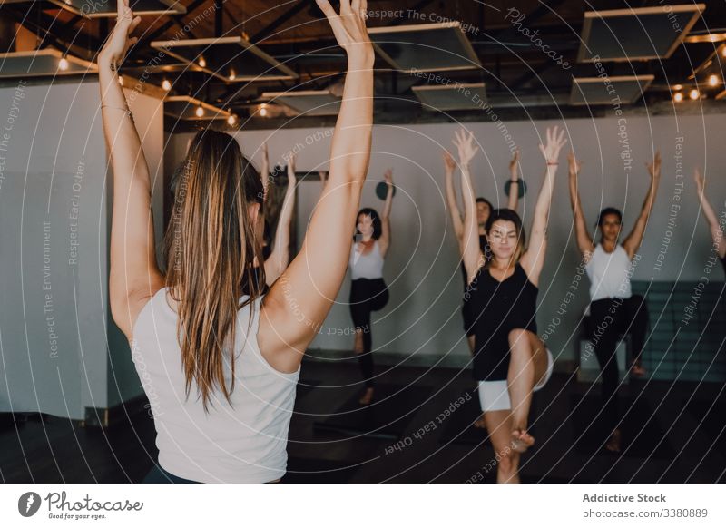 Gruppe von ruhigen, konzentrierten Frauen und Männern, die Yoga praktizieren, mit einem Trainer, der in Balance-Pose steht und den Körper im Studio dehnt