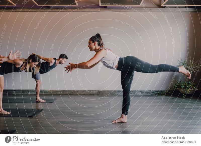 Erwachsene, die zusammen Yoga praktizieren, in Balance-Pose und Körperdehnung im hellen zeitgenössischen Studio Krieger-Pose Ausbilderin Übung üben