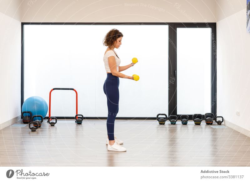 Fitnesstraining für Damen mit leichten Kurzhanteln im Fitnessstudio Frau Training Bizeps Locken Physiotherapie stehen schlank Muskel Athlet Übung Gesundheit
