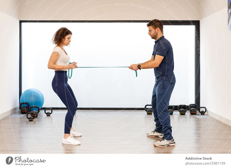 Frau und Mann trainieren gemeinsam mit Gummiband im Fitnessstudio Trainerin Physiotherapie Übung Wiederherstellung Gerät Zusammensein Widerstandskraft benutzend
