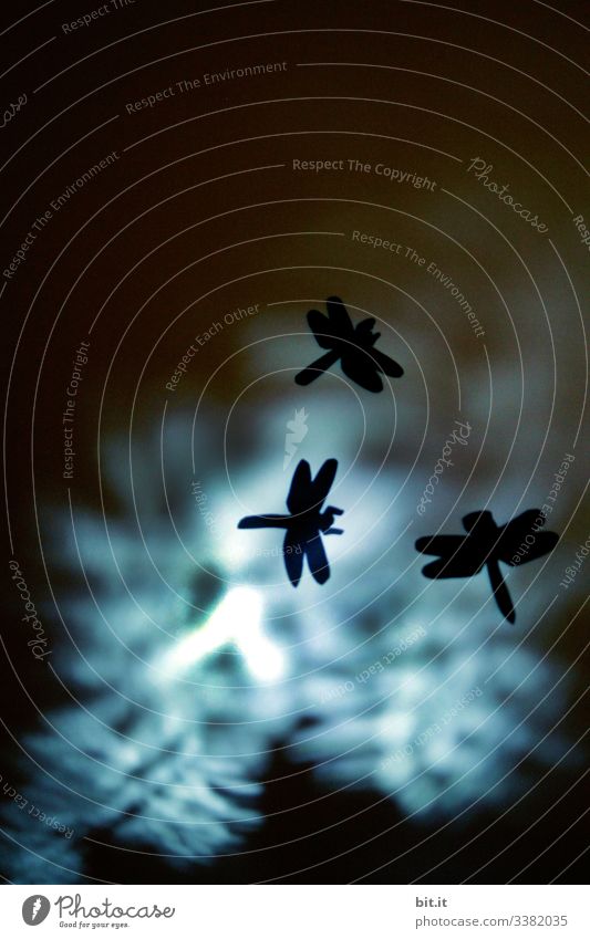 Libellentanz mit ausgeschnittenen Silhouetten von Libellen aus Tonpapier, vor strahlendem blauem und schwarzem Hintergrund.icht Lichtpunkt Schweben fliegen