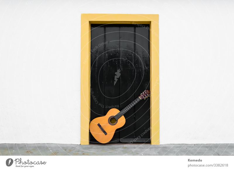 Spanische oder klassische Gitarre, die auf einer Tür eines andalusischen Innenhofes ruht. Außenaufnahme eines Musikinstruments in der weißen Wand eines Landhauses.