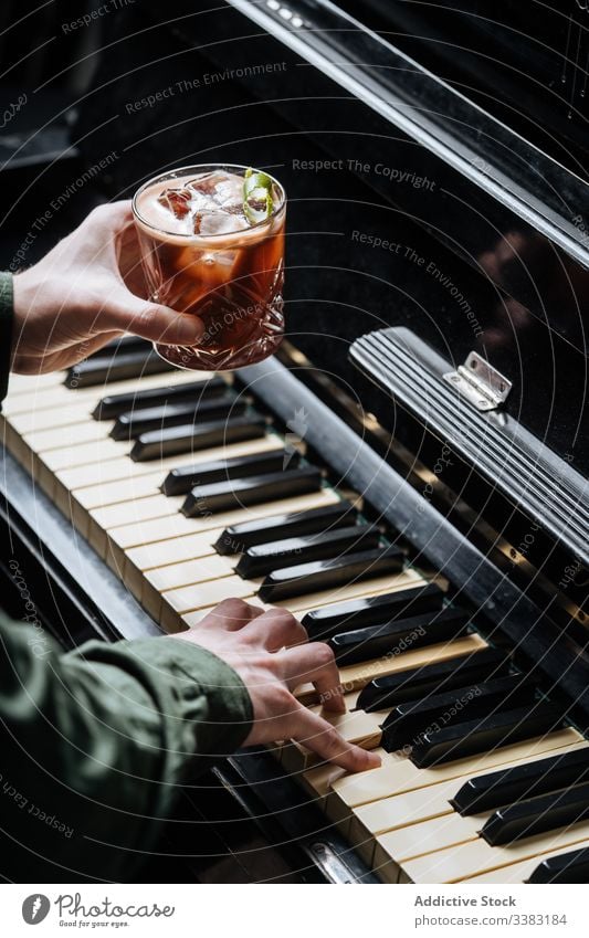 Unbekannter Mann übt Klavier mit einem Glas kaltem Getränk in der Hand spielen trinken Cocktail Pub Restaurant Bar Eis Minze schäumen professionell frisch