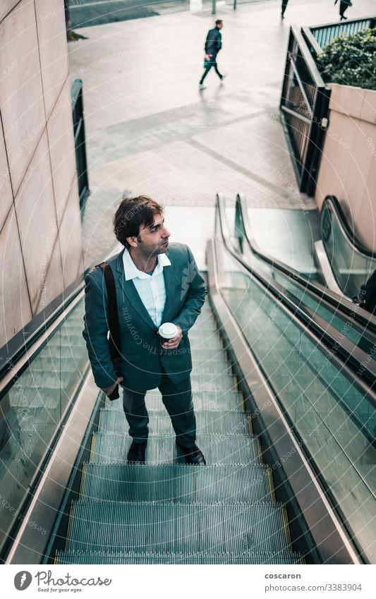 Geschäftsmann im Anzug, der einen Kaffee trinkt und eine Rolltreppe hinauffährt Erwachsener Flughafen attraktiv Chef Business Geschäftsleute Geschäftskleidung