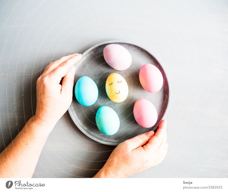 Hände halten einen Teller mit Ostereiern bemalt hand frau tisch grau draufsicht aufgemaltes gesicht humor lustig ostern teller Pastellfarben Foodfotografie