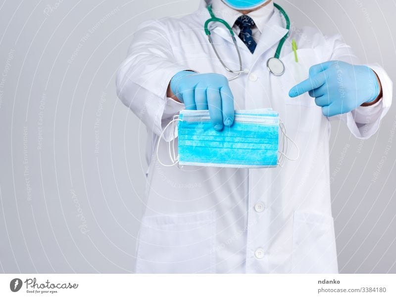 Arzt im weißen Kittel, blaue sterile Latexhandschuhe halten textile medizinische Masken in der Hand, Schutzzubehör gegen Viren Mundschutz Sanitäter Medizin