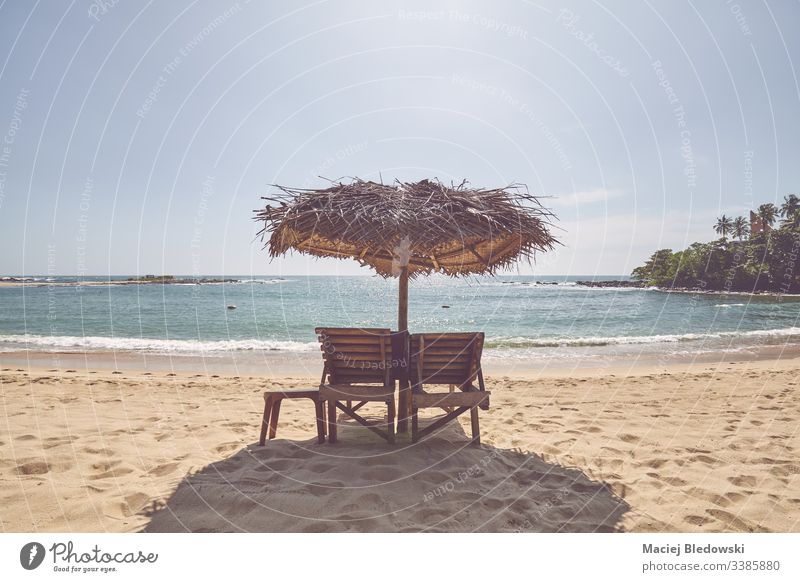 Hölzerne Sonnenbänke unter Palmblattschirm an einem tropischen Strand. Sommer Flucht Regenschirm Sonnenbank sich[Akk] entspannen friedlich Himmel Sand leer