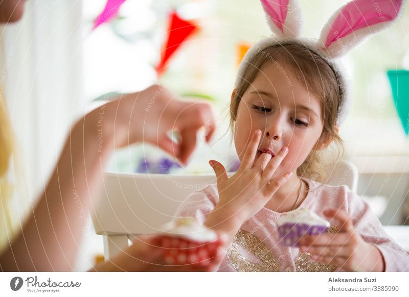 Mutter und Tochter feiern Ostern, kochen Muffins, mit Glasur überzogen. Fröhlicher Familienurlaub. Süßes kleines Mädchen in Hasenohren. backen offen Feier Kind