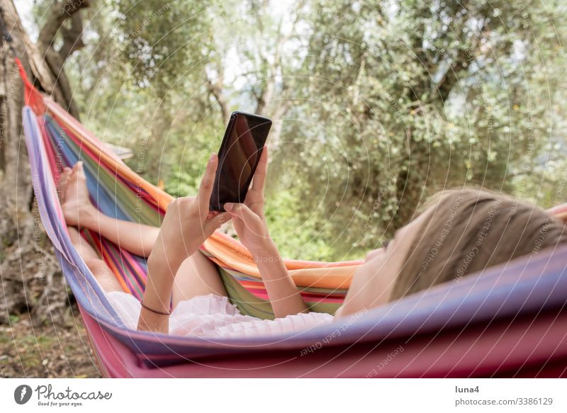 Mädchen mit smartphone liegt in Hängematte mädchen handy Urlaub fröhlich Ferien liegen erholen ausruhen lächeln Erreichbarkeit Natur glücklich lachen freude