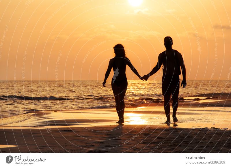 Silhouette eines Paares, das am Strand vor dem Sonnenuntergang spazieren geht laufen aktiv schön Küste konzeptionell nasser Sand Abend Feiertag Landschaft