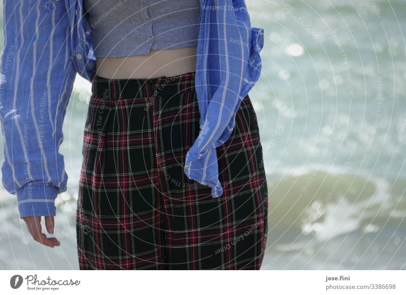 Junge Frau, Ausschnitt Oberkörper und Beine vor dem Meer Hemd kariert gestreift bauchfrei windig Hand Wellen blau Stoff Detailaufnahme Natur Sonnenlicht Sommer