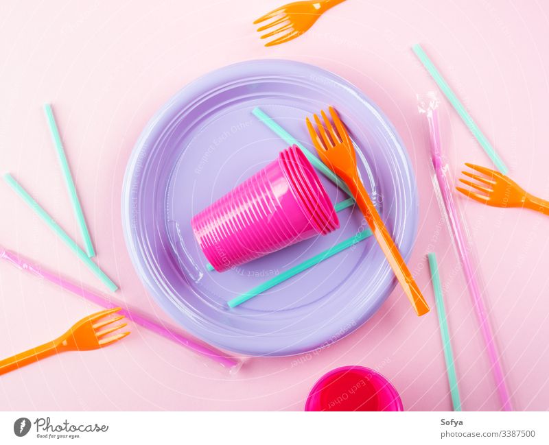 Bunte Einwegschale aus Kunststoff, Strohhalme und Tassen, Besteck. Flache Lage auf rosa Hintergrund. Einwegartikel Geschirr Speise farbenfroh Teller Verbot