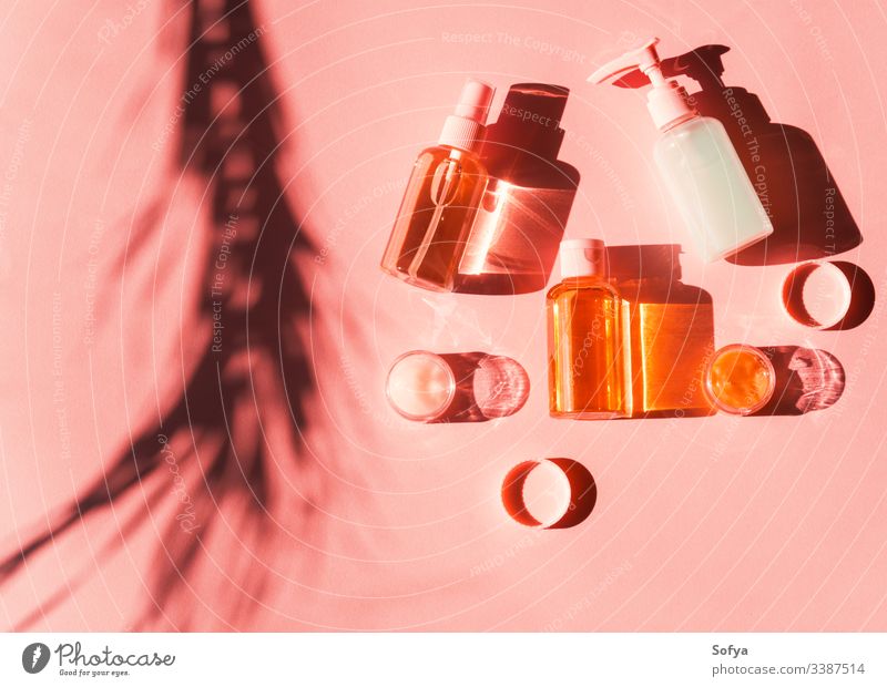 Verschiedene Kosmetikprodukte in Flaschen und Minidosen auf rosa Koralle. Flacher Schuss in hartem Licht mit Pflanzenschatten. Haut Produkte Schatten