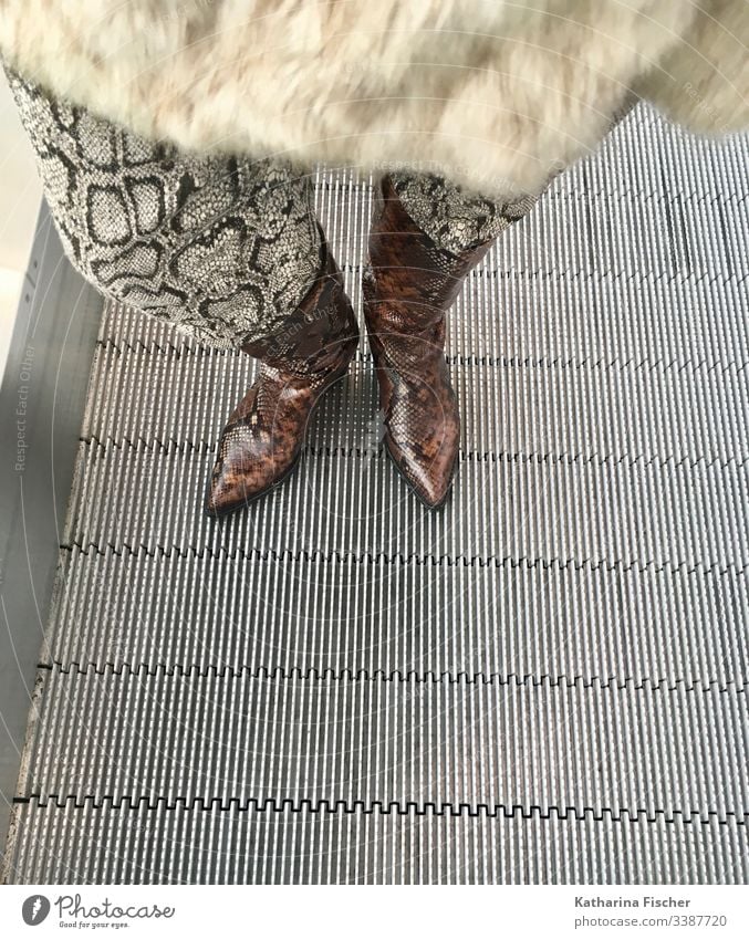 Stiefel Hose Schlangenoptik auf Rolltreppe Mode Schlangenmaserung Felljacke Leder Outfit stylisch stehen warten braun beige silber weiß Schuhe Farbfoto