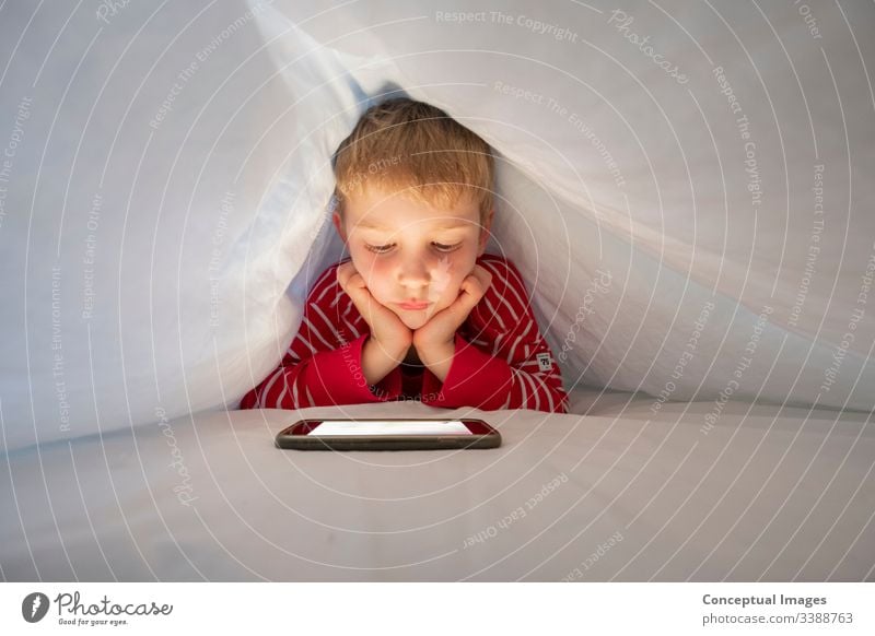 Kaukasischer Junge in seinem Bett, der mit seinem Smartphone einen Videoanruf macht, um mit einem Freund zu sprechen Kindheit facetime Mobile berühren