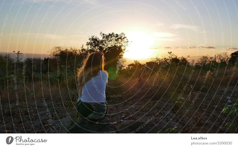 Eine Frau schaut sich sitzend auf einem Stein, den Sonnenuntergang an. Um Sie herum ist nur die Natur zu sehen. fernweh entspannen hoffnungsvoll neues natur