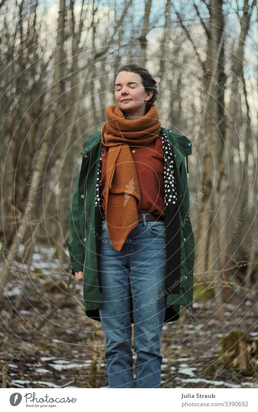 Frau steht im Wald mit geschlossenen Augen Bäume Wolken Mantel Schal hemdbluse Jeanshose gepunktet atmen geschlossene Augen Gürtel ockerfarben Grün