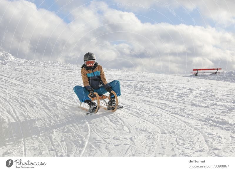 Junge auf Schlitten in Schneelandschaft Rodel rodeln schlittenfahren lustig schnell Winter Abfahrt Spaß kalt aussen draußen Vergnügen Piste Winterwonderland
